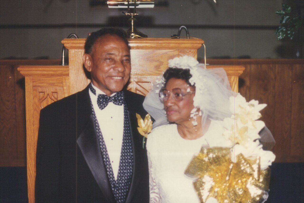 An older couple poses for a photo in wedding attire.