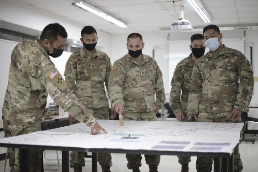 Five service members stand around a table looking at documents.