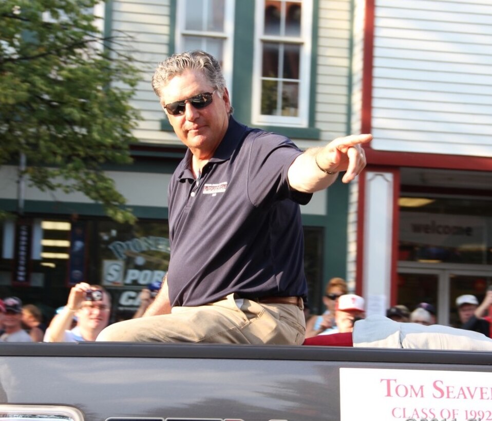 A man sits elevated above a crowd and points at something in the distance.