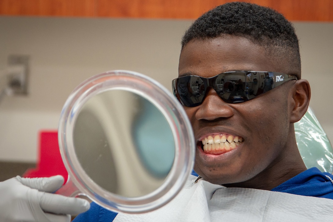 A Marine patient wearing dark glasses smiles while looking into a mirror.