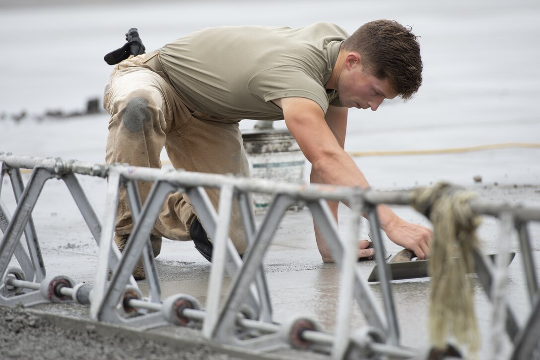 Airman 1st Class Josiah Gomberg, 823d RED HORSE Squadron pavement and equipment construction journeyman, levels wet concrete as part of a construction project to expand a flightline apron June 30, 2021, at Yokota Air Base, Japan. Airmen assigned to the 823rd, 819th and 820th RED HORSE Squadrons, combined efforts to increase aircraft parking capabilities. The apron expansion is the first in an approximately four-year phased construction effort to enhance Yokota Air Base’s airlift mission and is the first 800th RED HORSE Group project within the U.S. Indo-Pacific Command. (U.S. Air Force photo by Tech. Sgt. Christopher Hubenthal)