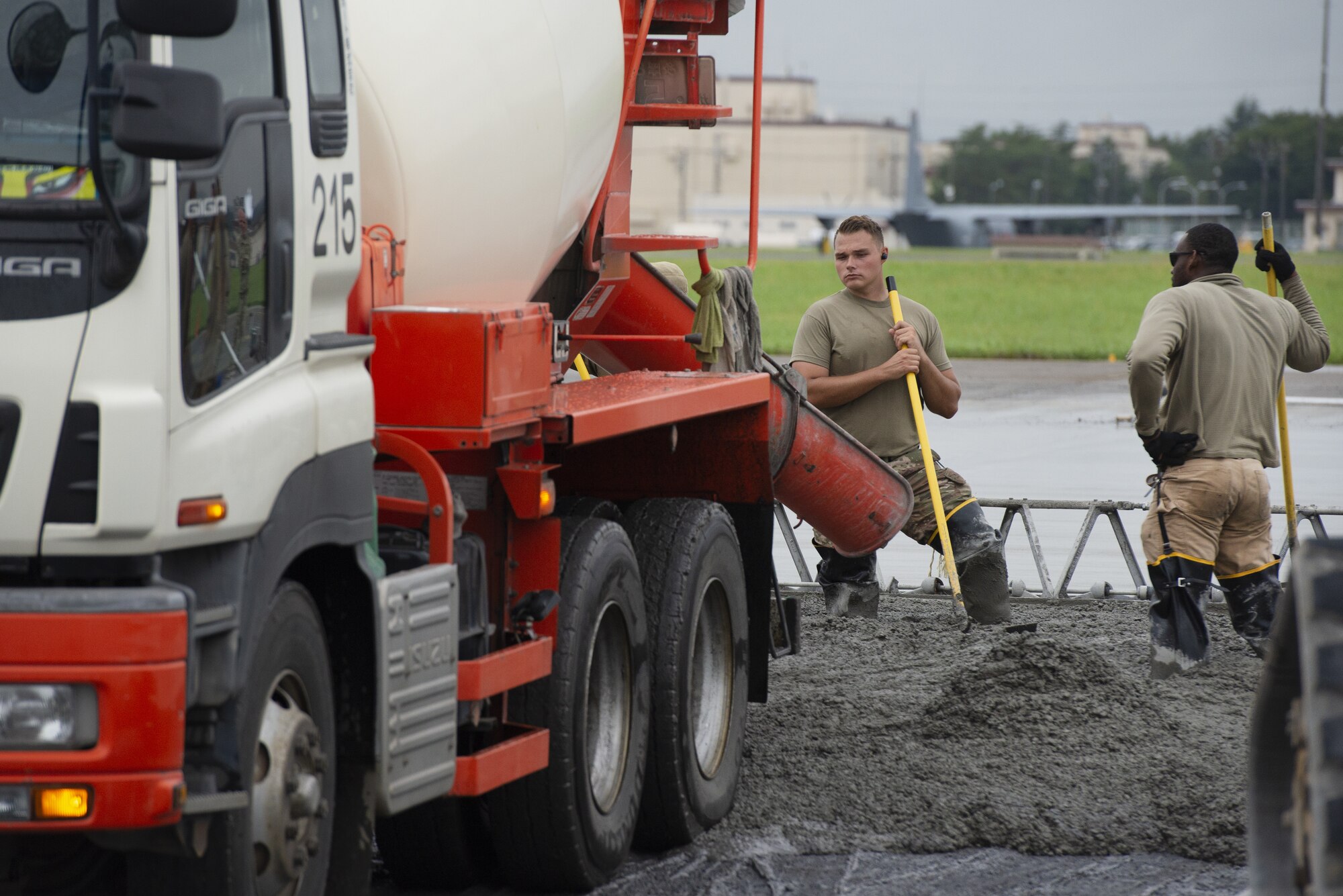 Senior Airman Kendall Allison, center, 819th RED HORSE Squadron structural journeyman, and Staff Sgt. Kelvin Grover, right, 823rd RED HORSE Squadron structural craftsman, lay down wet concrete as part of a construction project to expand a flightline apron June 30, 2021, at Yokota Air Base, Japan. The construction project is the first 800th RED HORSE Group project within the U.S. Indo-Pacific and is led by the 823rd RED HORSE Squadron with support from the 819th and 820th RED HORSE Squadrons. The apron expansion is the first in an approximately four-year phased construction effort to enhance Yokota Air Base’s airlift mission capabilities. (U.S. Air Force photo by Tech. Sgt. Christopher Hubenthal)