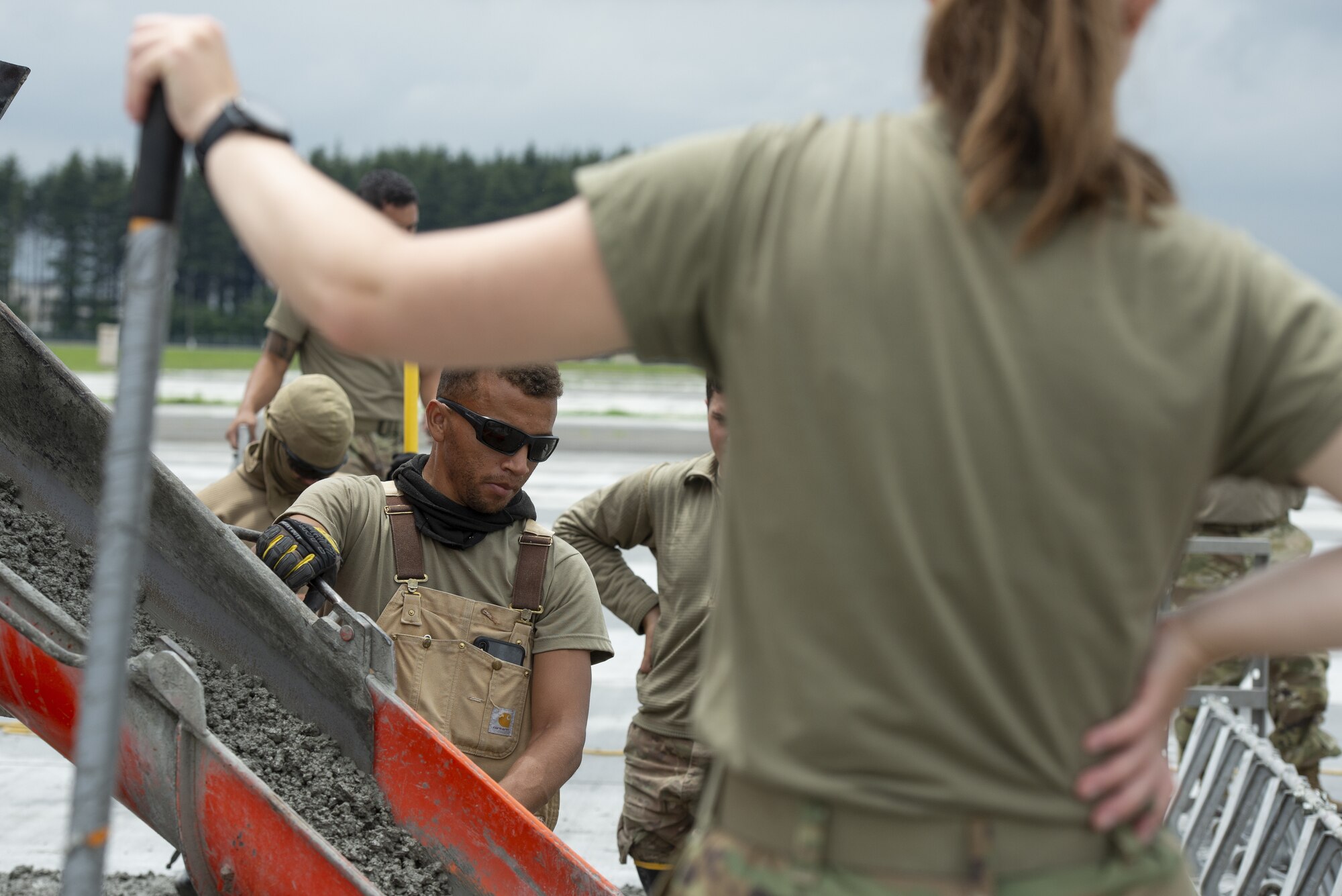 Staff Sgt. John McCardy, 823rd RED HORSE Squadron pavement and construction equipment craftsman, distributes wet concrete as part of a construction project to expand a flightline apron June 30, 2021, at Yokota Air Base, Japan. The construction project requires Airmen assigned to the 823rd, 819th and 820th RED HORSE Squadrons to pour approximately 7,300 cubic meters of concrete and pave 650 tons of asphalt in a construction project meant to increase aircraft parking capabilities at Yokota Air Base. The apron expansion is the first in an approximately four-year phased construction effort to enhance Yokota Air Base’s airlift mission capabilities. (U.S. Air Force photo by Tech. Sgt. Christopher Hubenthal)