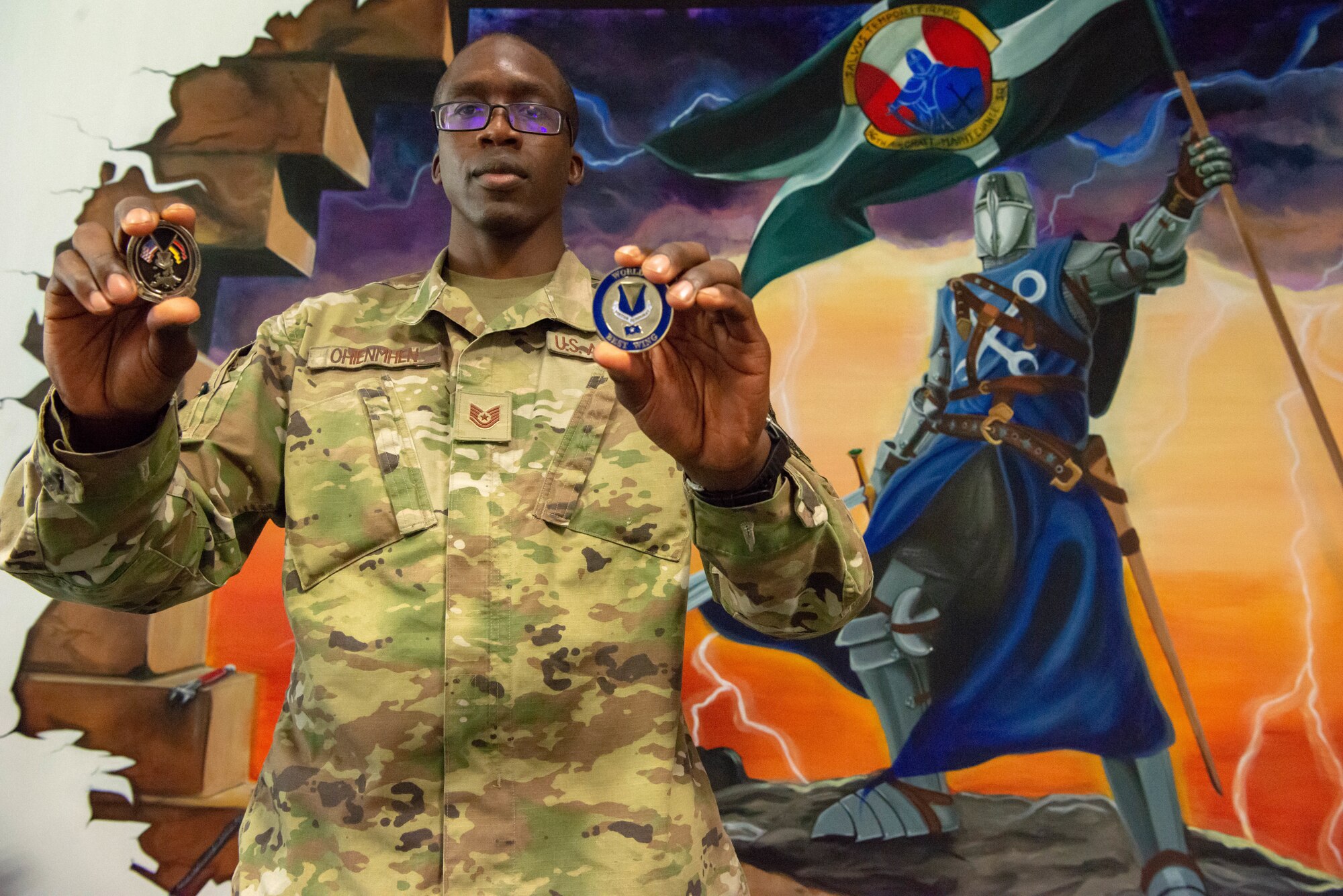 Airman holds up coins next to picture of knight.