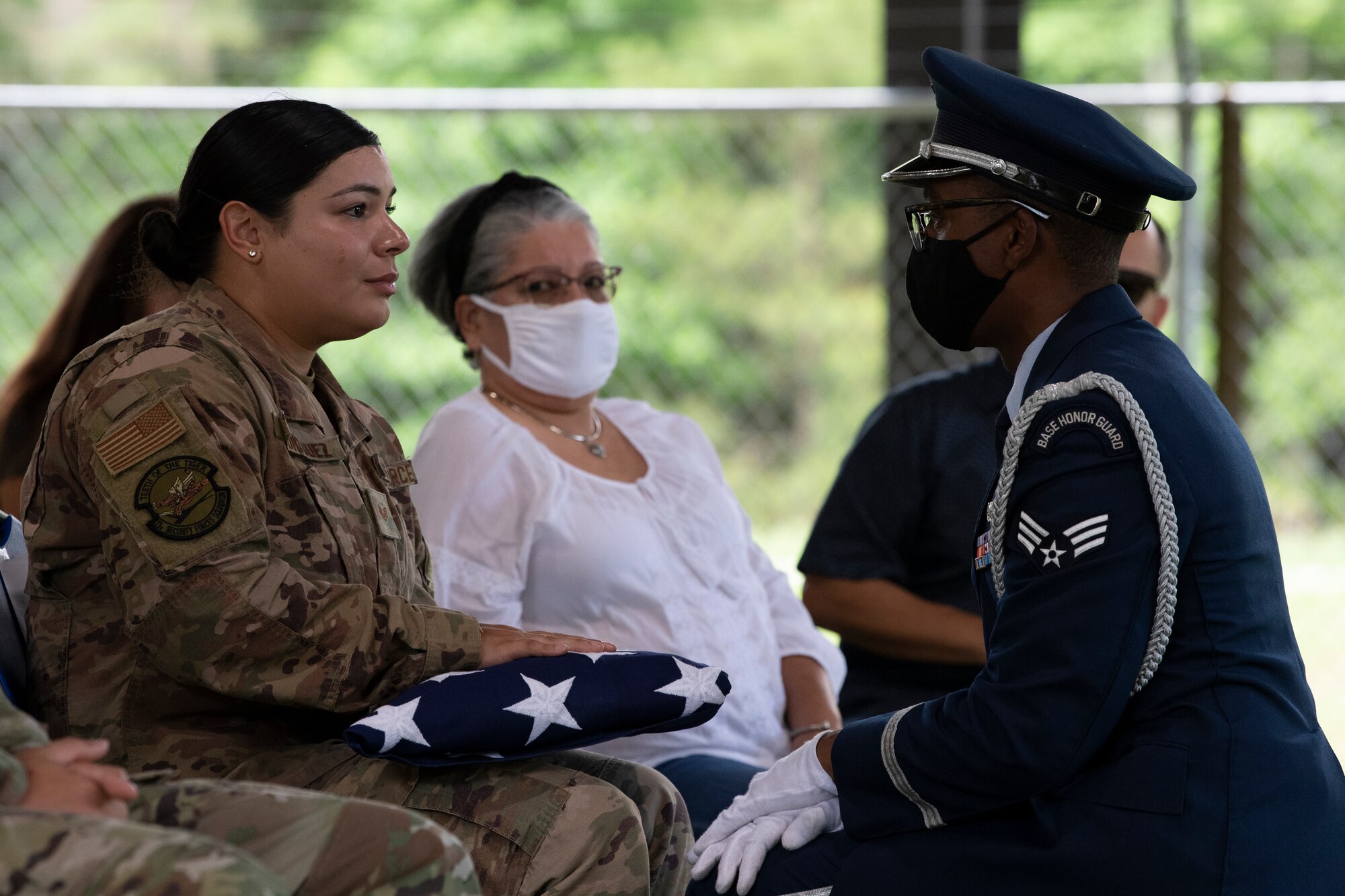 A photo of an honor guard member kneeling down in front of a woman Airman who is holding a ceremonial flag.