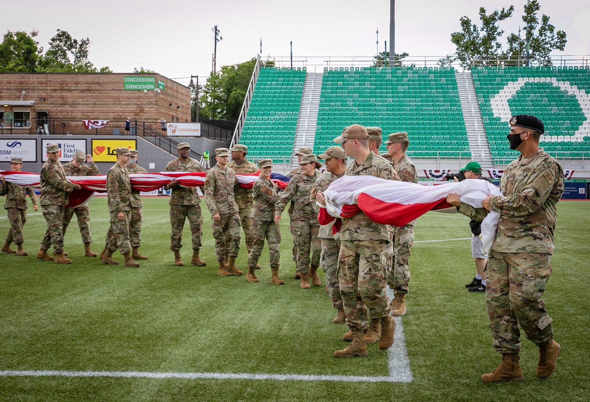 Airmen carry out large U.S. flag on soccer field.
