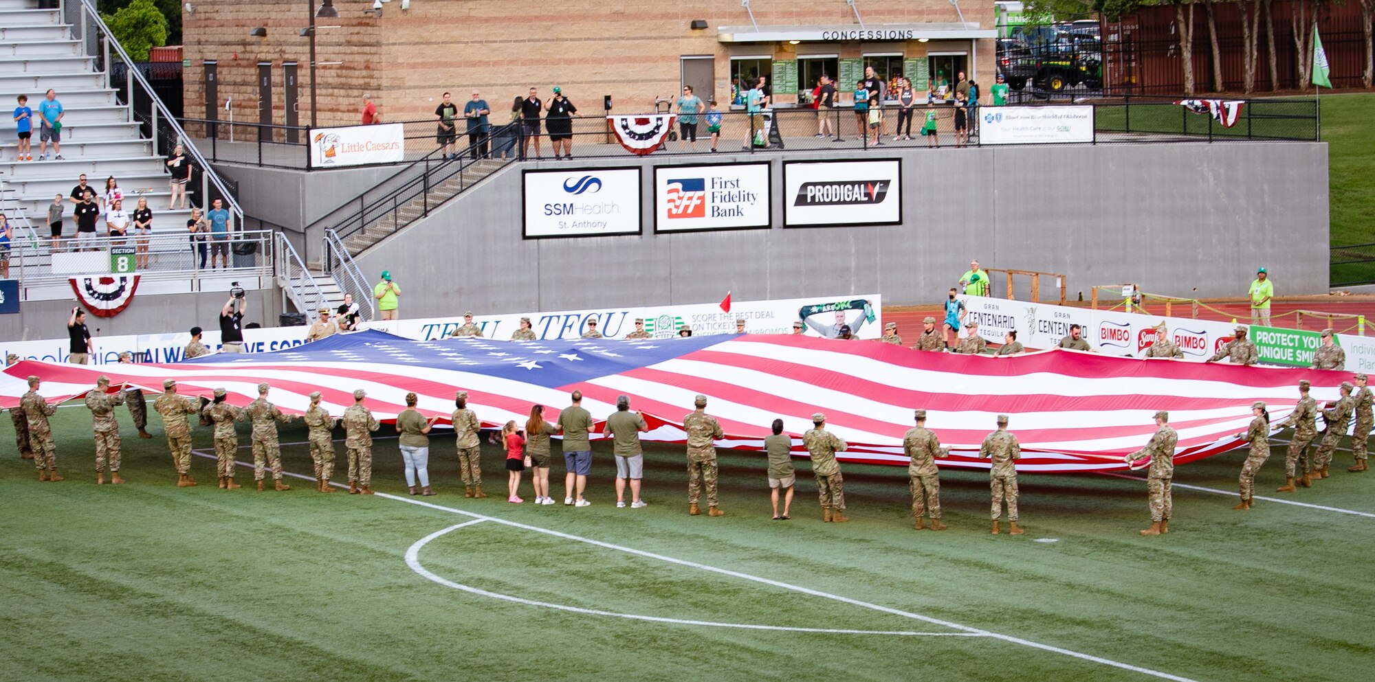 Airmen unfurl large U.S. flag on soccer field.