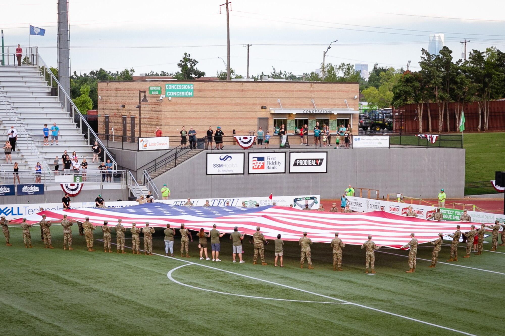 Airman unfurling large U.S. flag on soccer field.