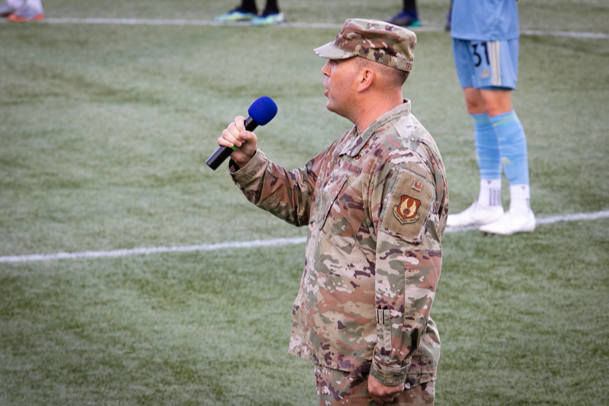 Air Force Colonel singing National Anthem on field.
