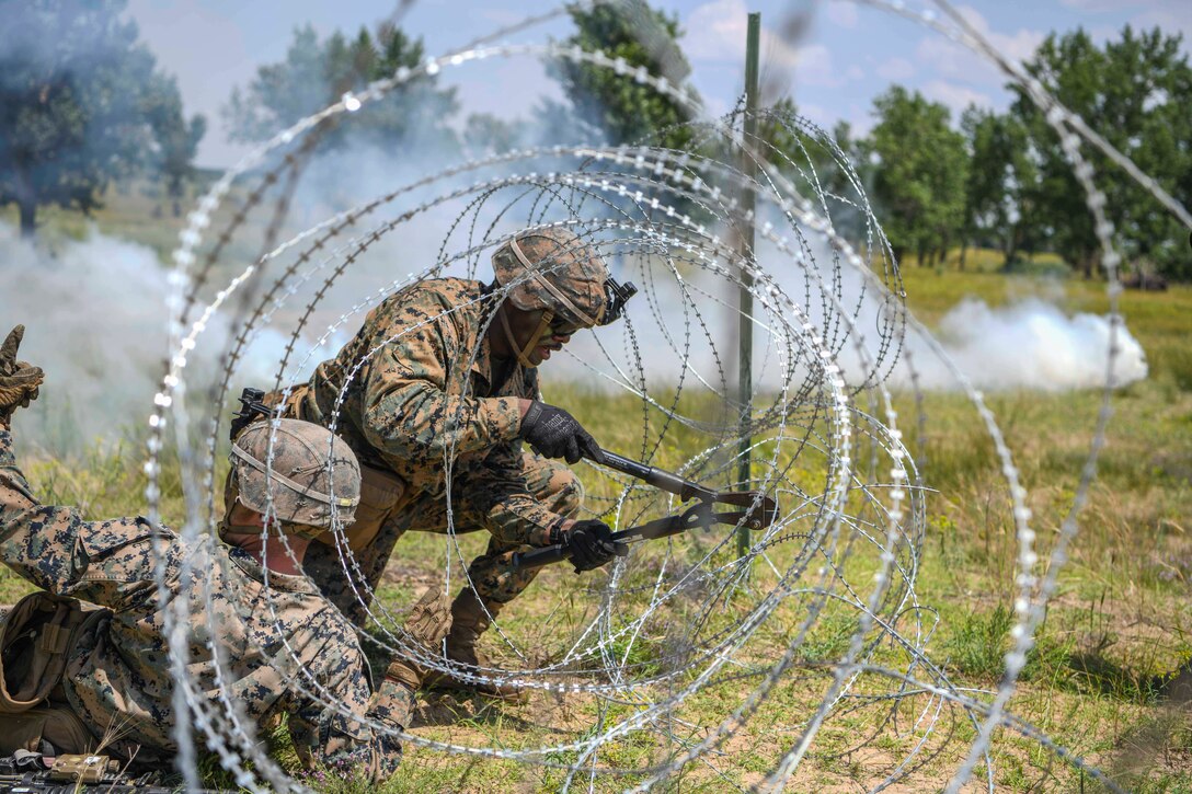 Marines use a tool to cut through a barbed wire fence.