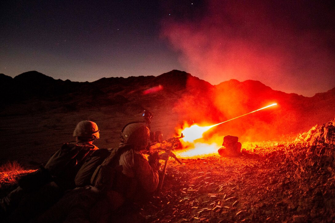 Marines fire a machine gun at night.