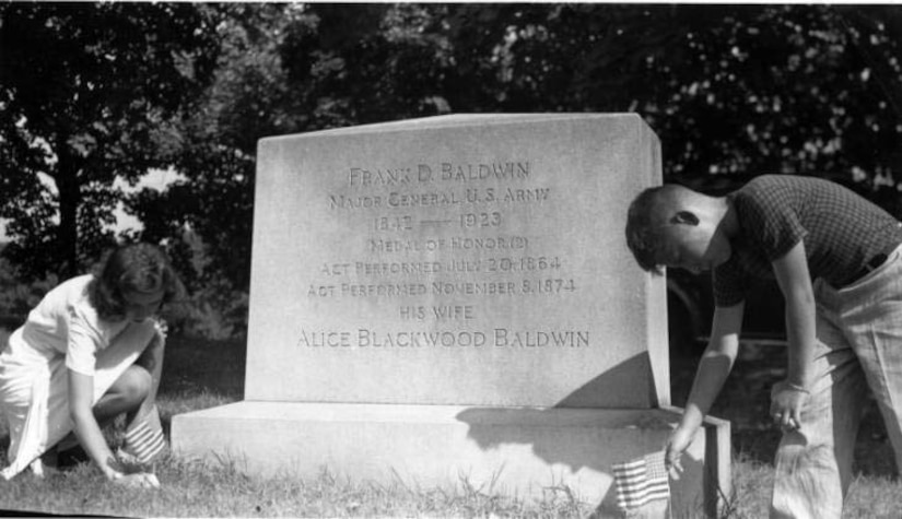 A boy and a woman place small American flags at a grave marker.