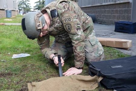 u.s. army soldier uses a knife to lift a piece of cloth.