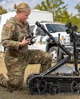 woman in uniform kneels by a robot.