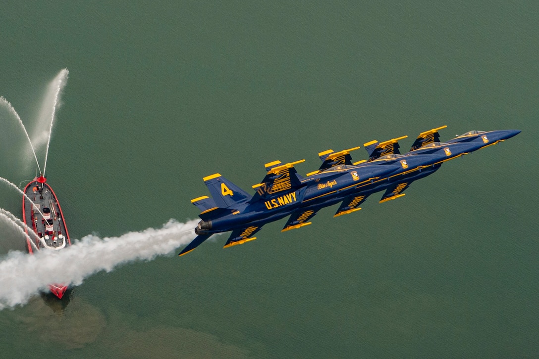 Aircraft fly in formation over a ship transiting a body of water.