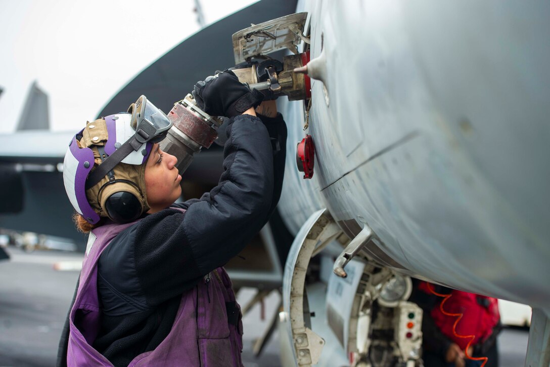 A sailor connects a fuel pump to an aircraft.