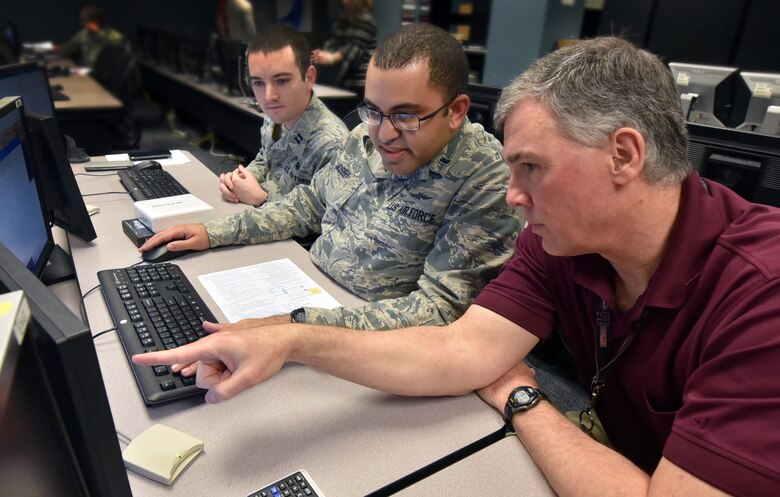 Capt. Seth Martin and 1st Lt.Joshua Mosby, Air Force Institute of Technology students, listen as Barry Mullins, AFIT computer engineering professor, explains a hacking technique they can use during their computer systems cyberattack class at Wright-Patterson Air Force Base, Ohio, Feb. 20, 2018. Counter insurgency hacking is an espionage attack weapon taught to deter enemy threats to national computer communication systems. (U.S. Air Force Photo by Al Bright/Released)