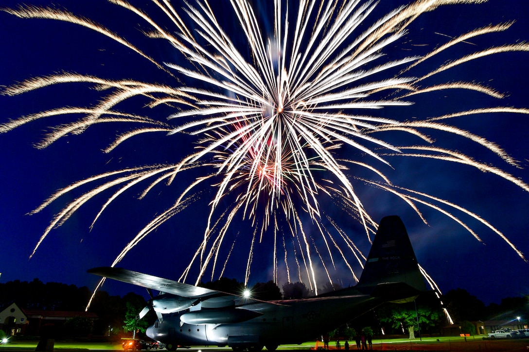 Fireworks light up the sky above a military aircraft.