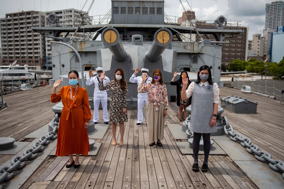 Seven men and women hold up their right hands outdoors on a ship.
