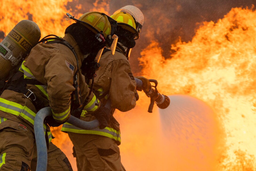 Air Force firefighters use a water hose to put a fire.