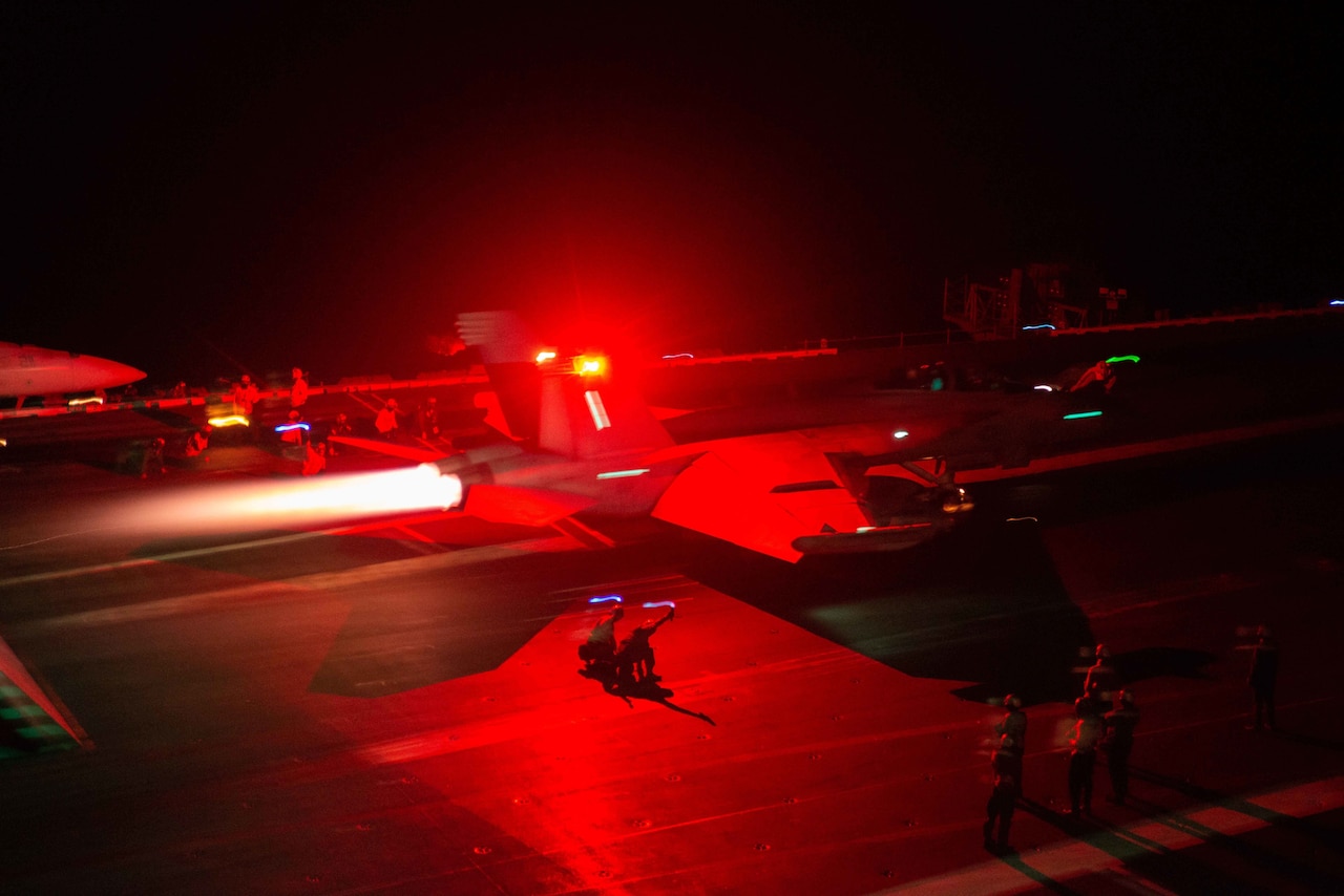 A jet takes off from a carrier at night.