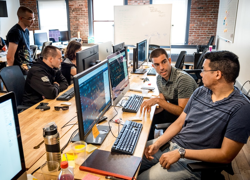 Senior Airman Sean Armstrong, software engineer, and Maj. Drew Armstrong, right, a data scientist, discuss a software development project at the office of Kessel Run, a program within the Defense Innovation Unit Experimental, a United States Department of Defense organization, in Boston May. 30, 2018. Air Force software coders have been learning private sector techniques, such as coding in an open environment to encourage constant collaboration and communication, in order to deliver software solutions to the warfighter in weeks and months instead of years. (U.S. Air Force photo by J.M. Eddins Jr.)