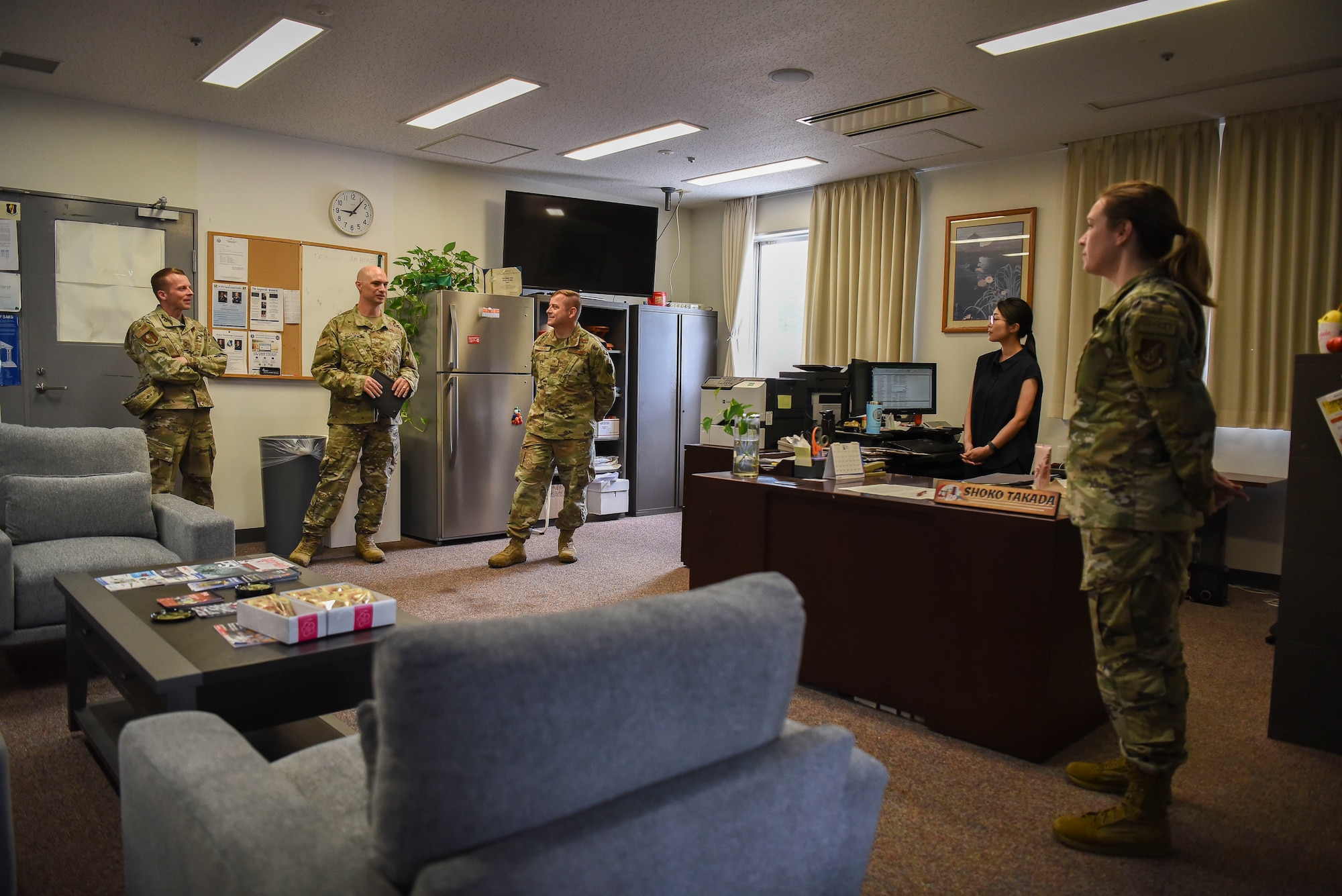 A group of military members are in an office listening to the center one near the door speak.