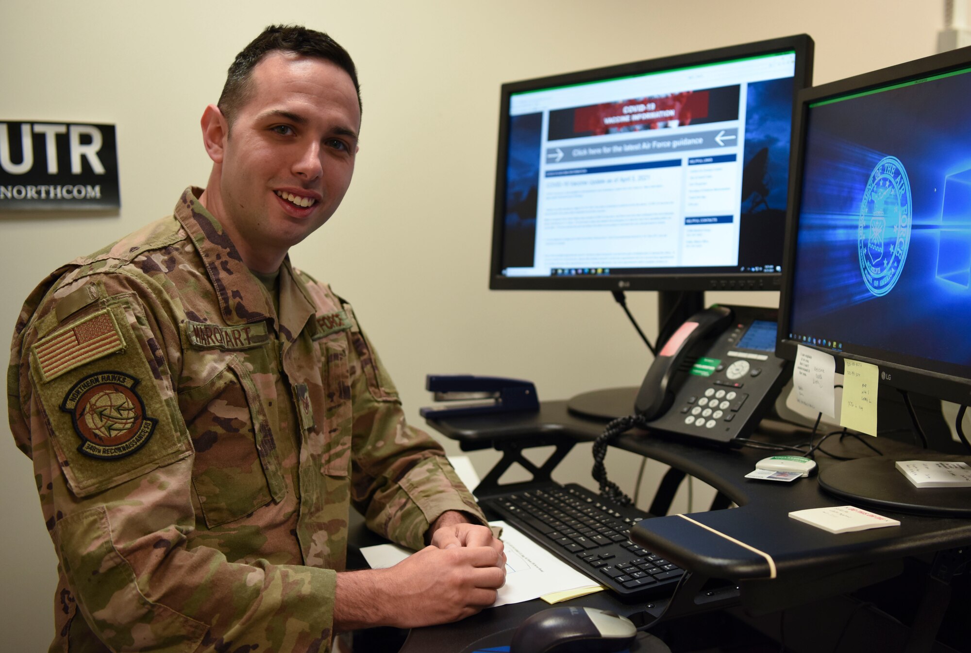 Airman stands next to computer and smiles at camera.