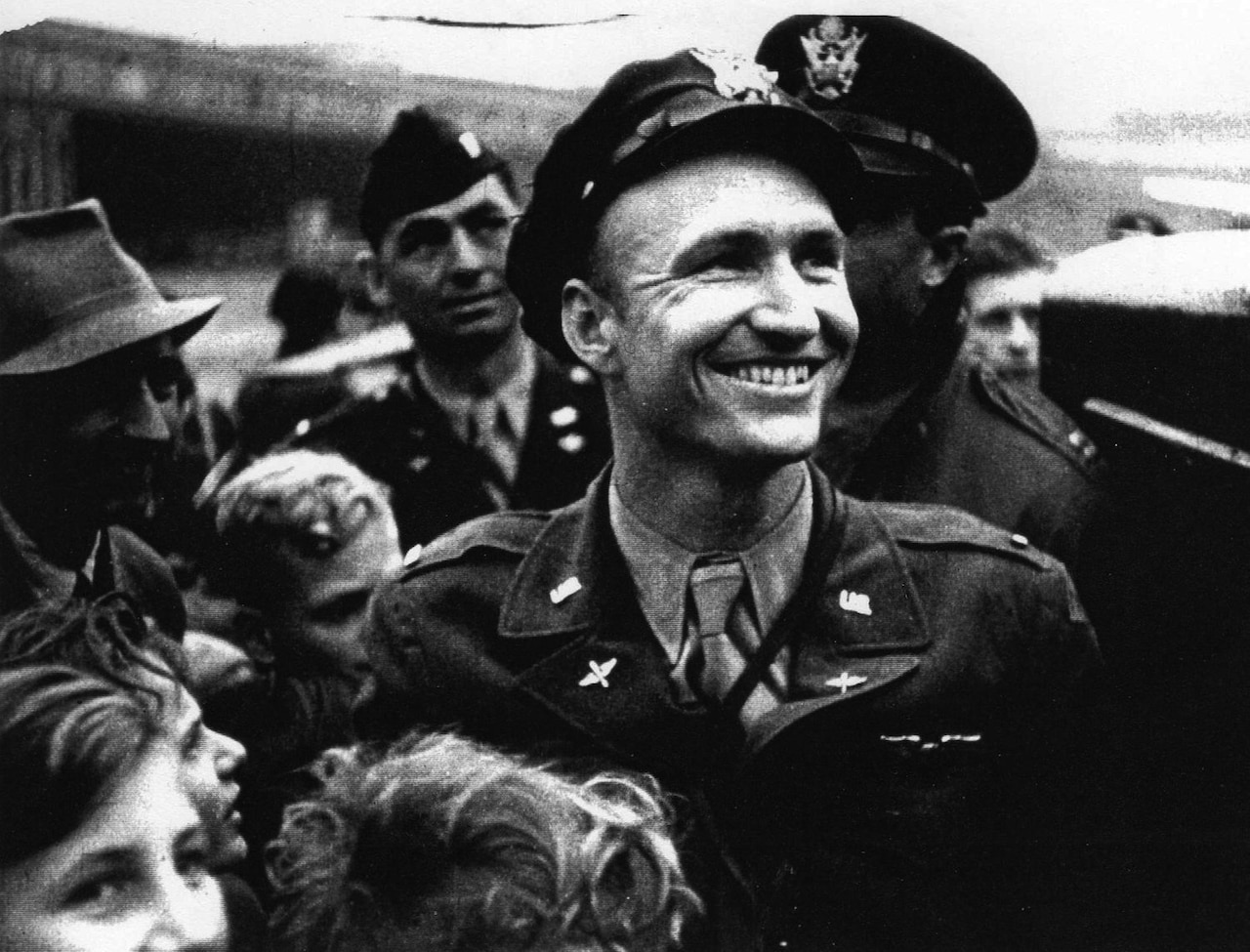 A pilot smiles while surrounded by children.