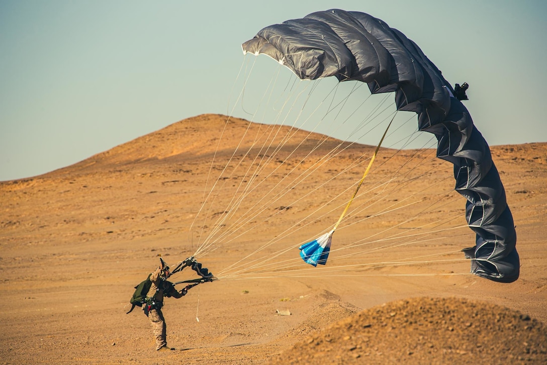 A Marine holds onto to a large parachute after landing in the desert.