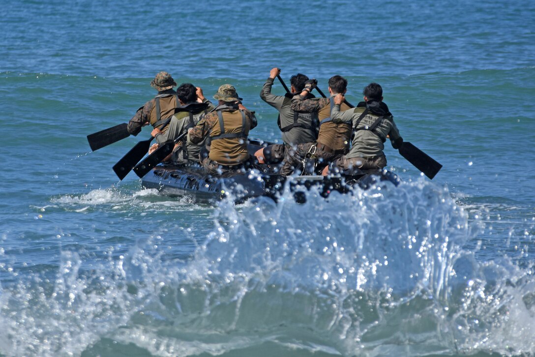 Marines paddle a large rubber raft away from the camera.