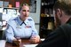 Airman in blues leans on desk while explaining a document to a civilian sitting across from her.