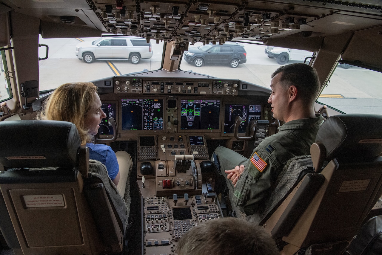 A woman talks to service members in the cockpit of an airplane on the tarmac.