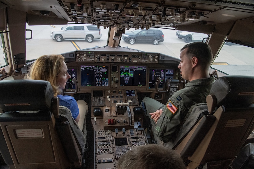 A woman talks to service members in the cockpit of an airplane on the tarmac.
