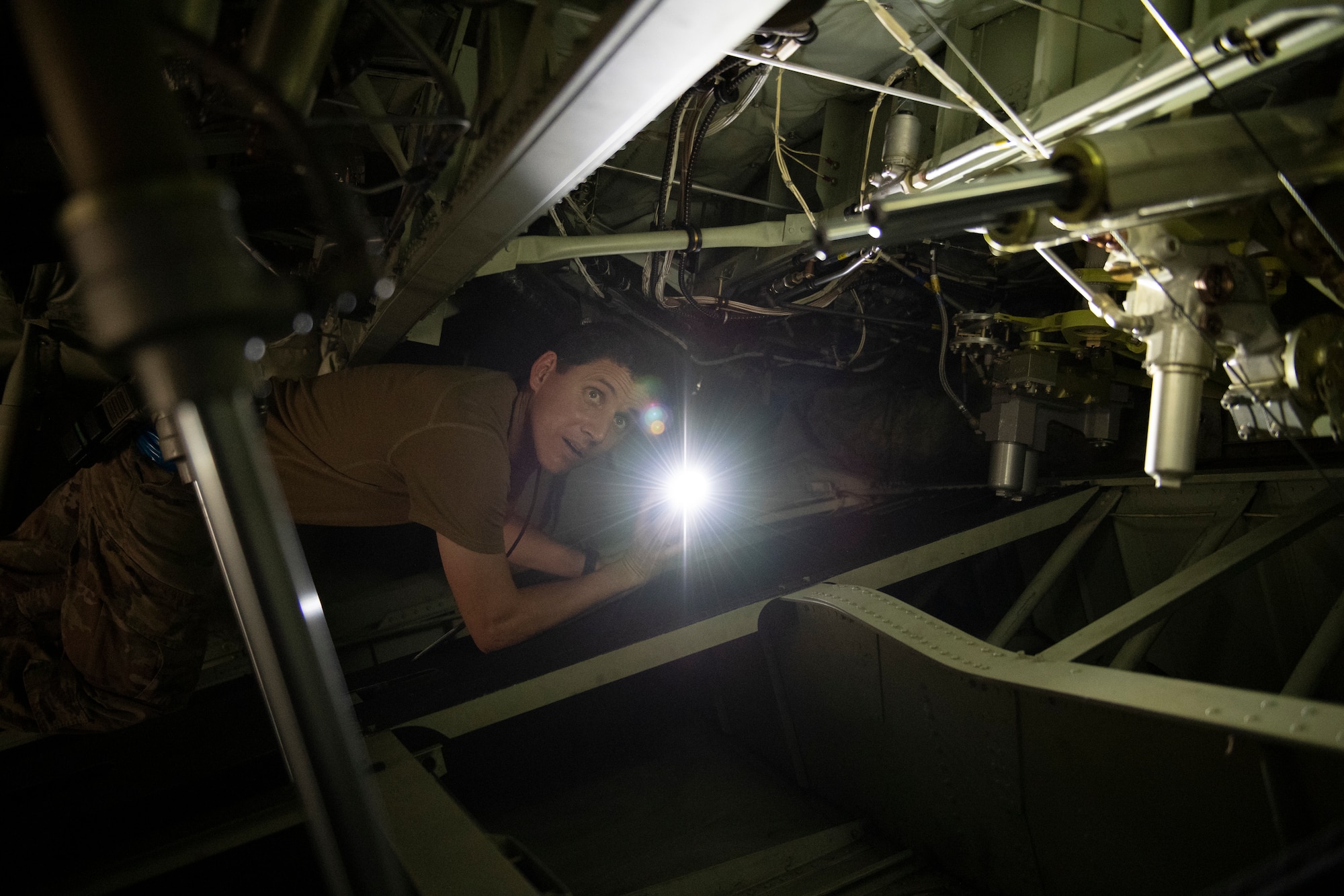 A photo of an Airman pointing a flash light at wires in an HC-130J Combat King II.