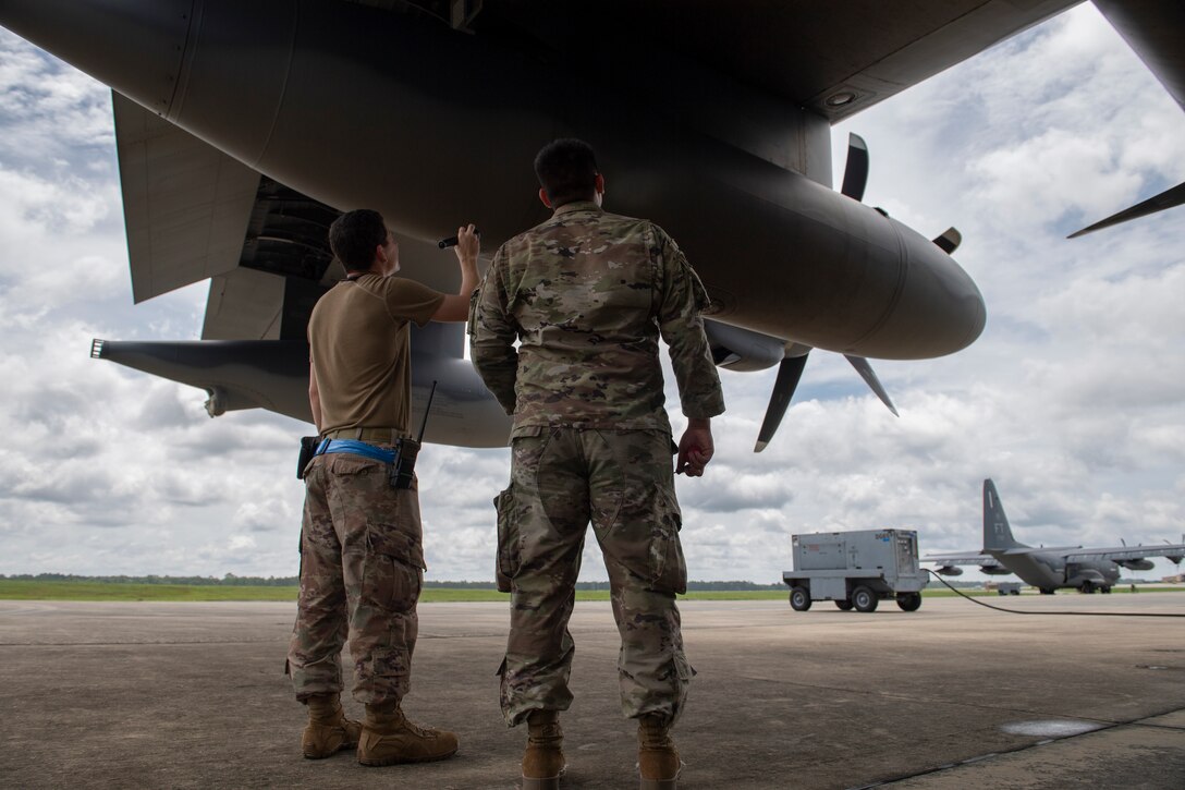 A photo of two Airmen standing under the wing of a HC-130J Combat King II aircraft and one of them is pointing a flashlight up under the wing.