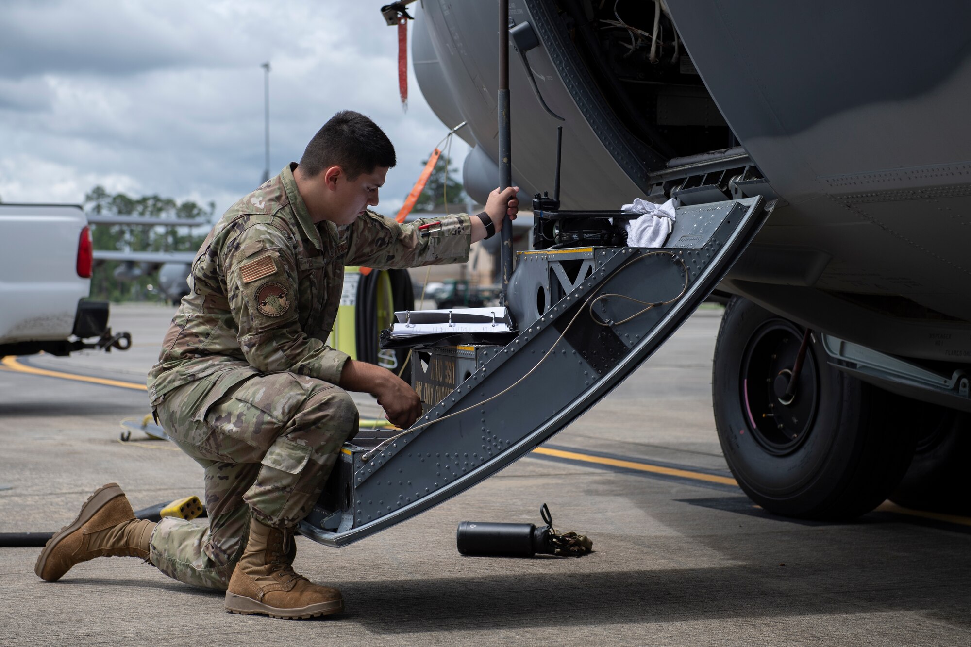 A photo of an Airman kneeling next to a door on a C-130 while looking at a binder on the steps in front of him.