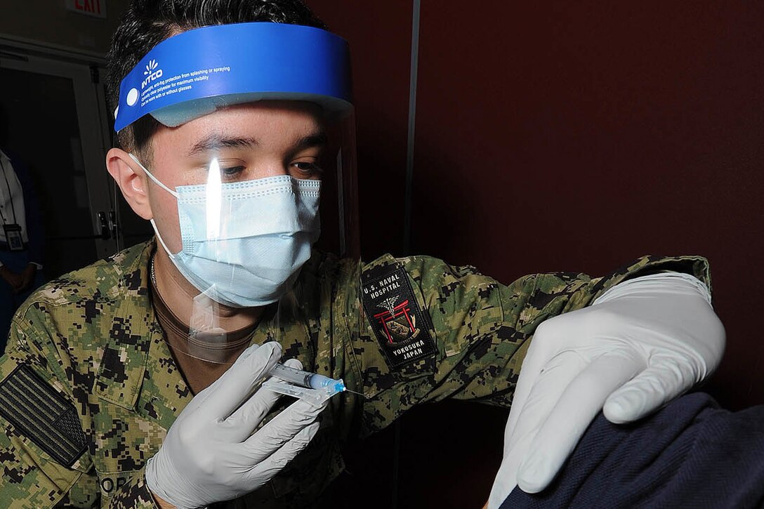 A sailor wearing a face mask gives a shot to a civilian.