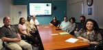 IMAGE: Cybersecurity and Compliance Branch Assessment and Authorization (A and A) Lead Barney Mahaney is briefing members of his team regarding risk management framework packages for various warfare systems. Pictured seated from left to right clockwise is Navy Validator Jack Owens, Corporate Package Information System Security Officer Denayja Boone, Corporate Package A and A Calvin Brown, Cybersecurity and Compliance Branch A & A Lead Barney Mahaney, Cybersecurity Engineer Laura Allen, Navy Validator Kenneth Roe, IT Specialist Nikita Robinson, Navy Validator Jean Ragsdale and Senior Systems Security Engineer and A and A Lead Angie Pierce.