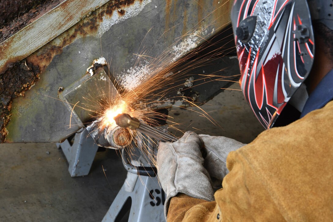 An airman uses a torch on a staircase as sparks fly.