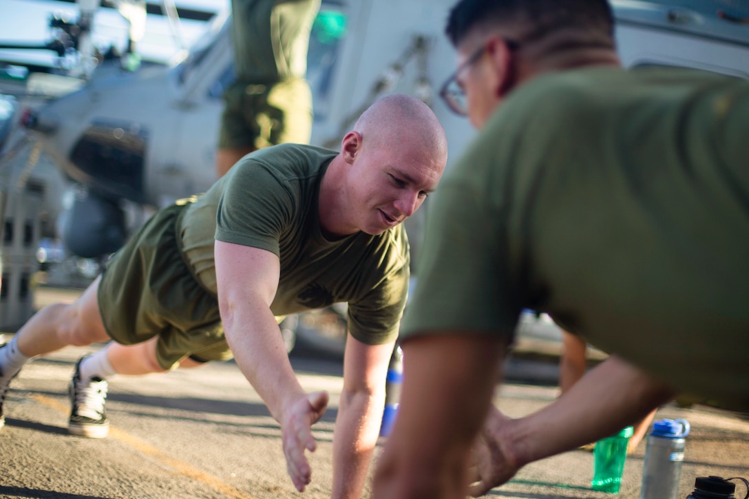 Two Marines high five each other while performing pushups on a ship.