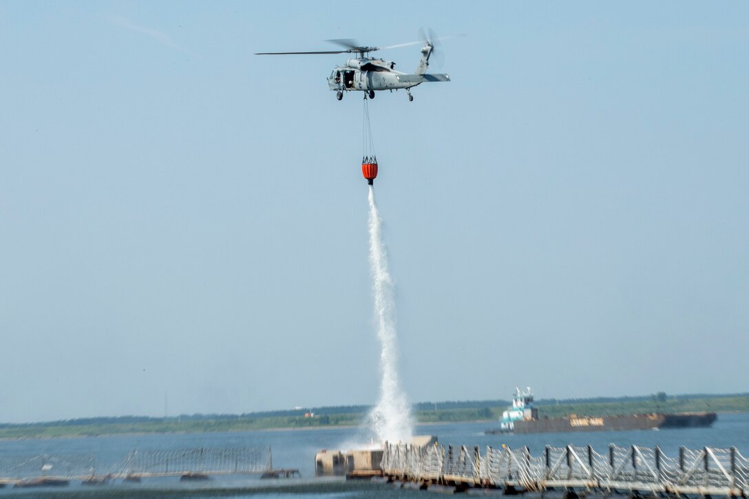A helicopter releases water from a bucket over a body of water.