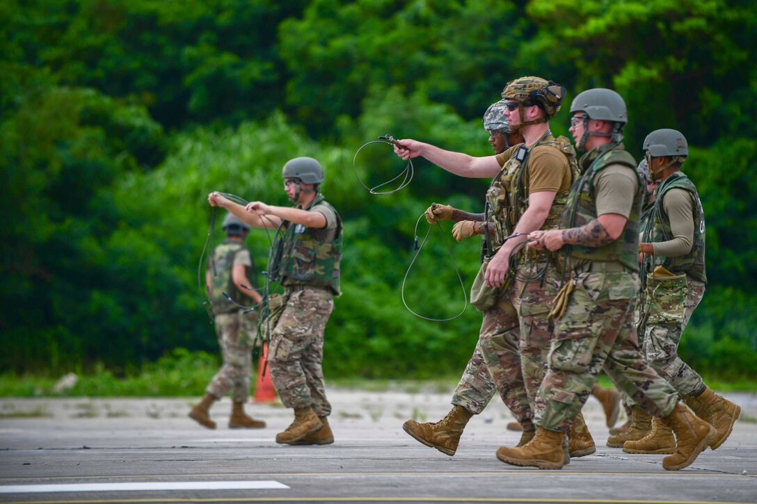 Airmen walk as a group while holding cables.