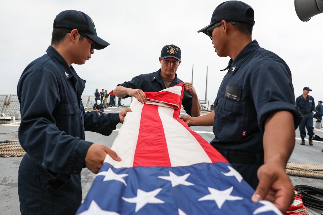 Three sailors fold an American flag on a ship.