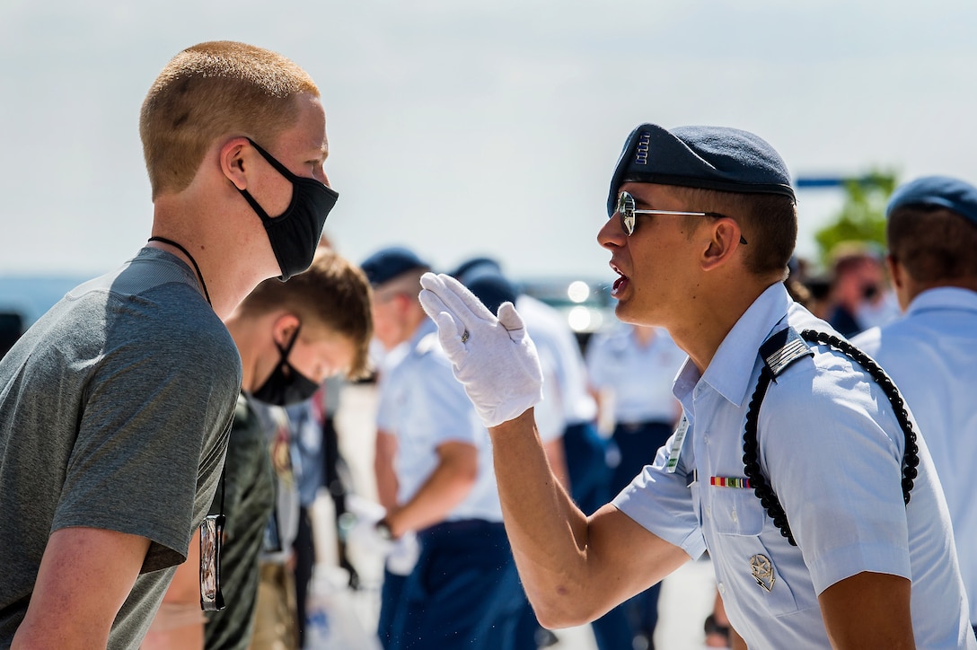 An airman wearing a white glove talks animatedly with another with others in the background.