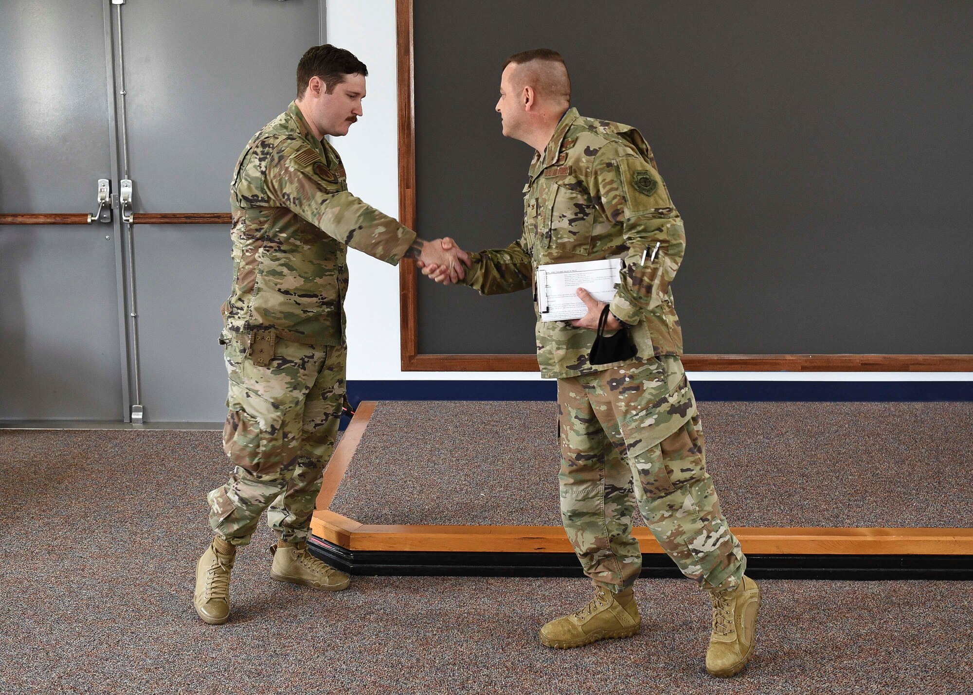 Two military members shake hands. The member on the right coins the one on the left in the hand shake.