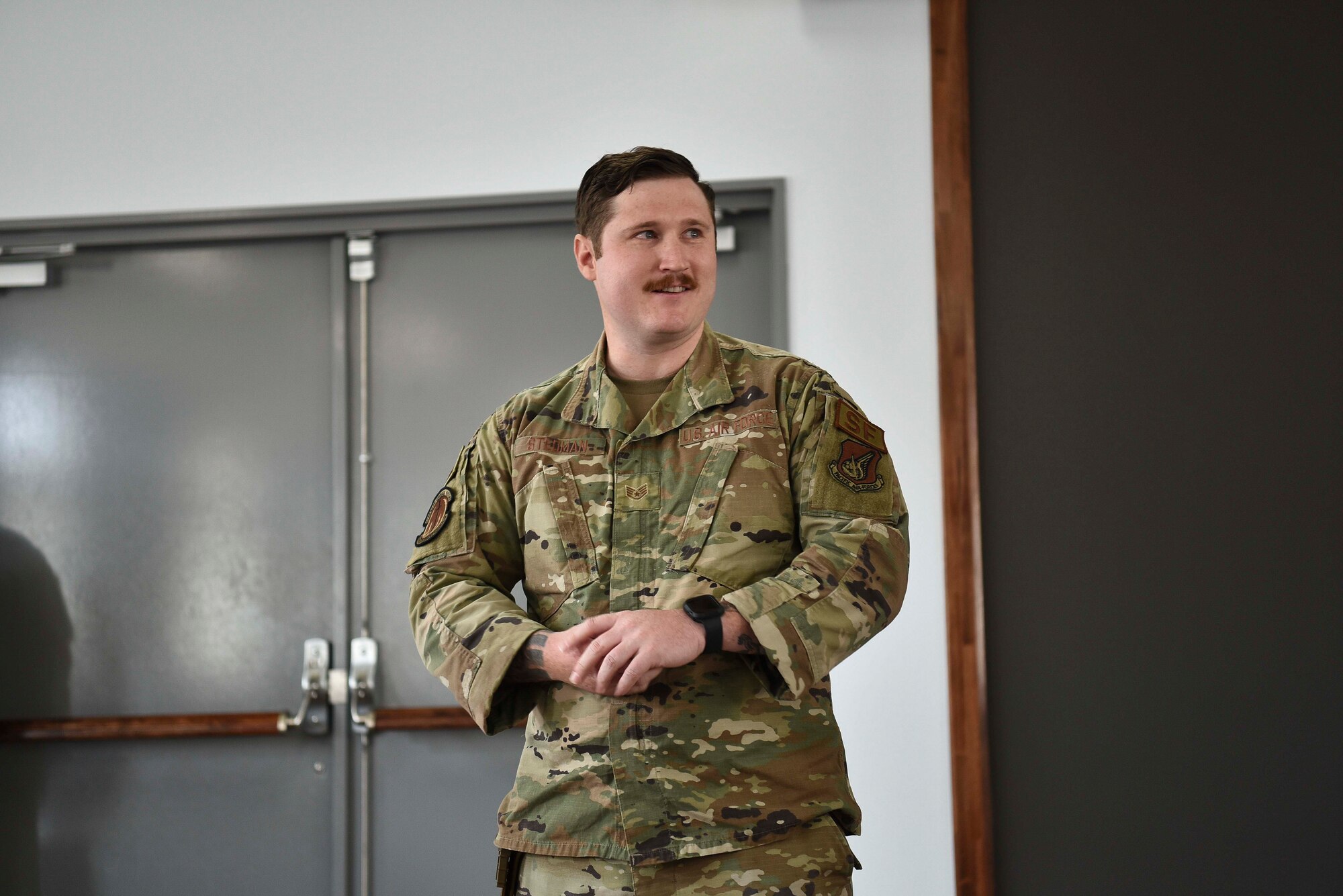 A military member holds his hands as he stands in front of a room.