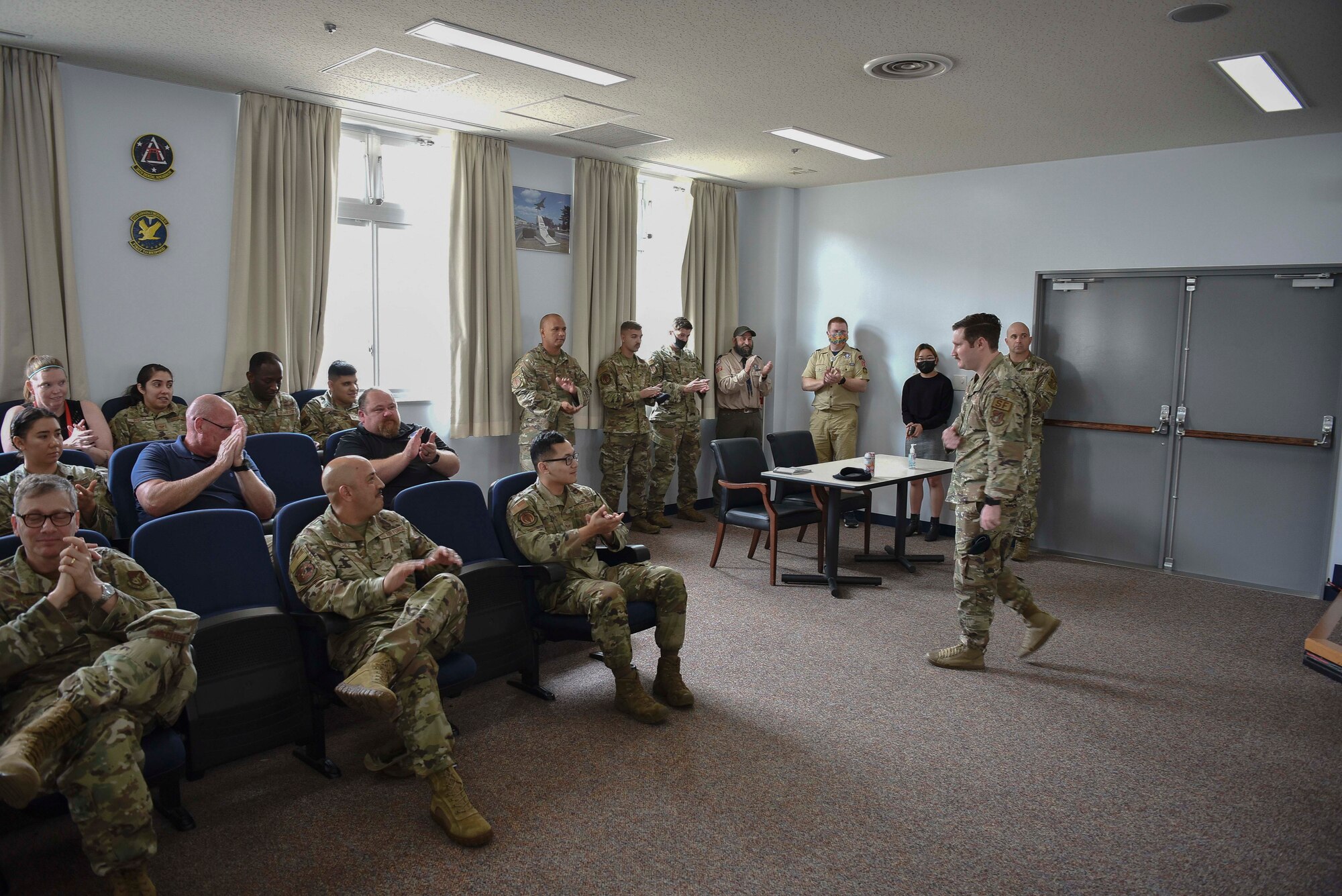 A military member walks across a room as others in the room clap for him.
