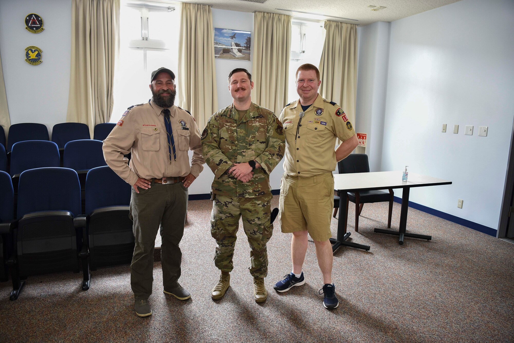 A military member stands in between two Cub Scout masters as the three pose for a picture