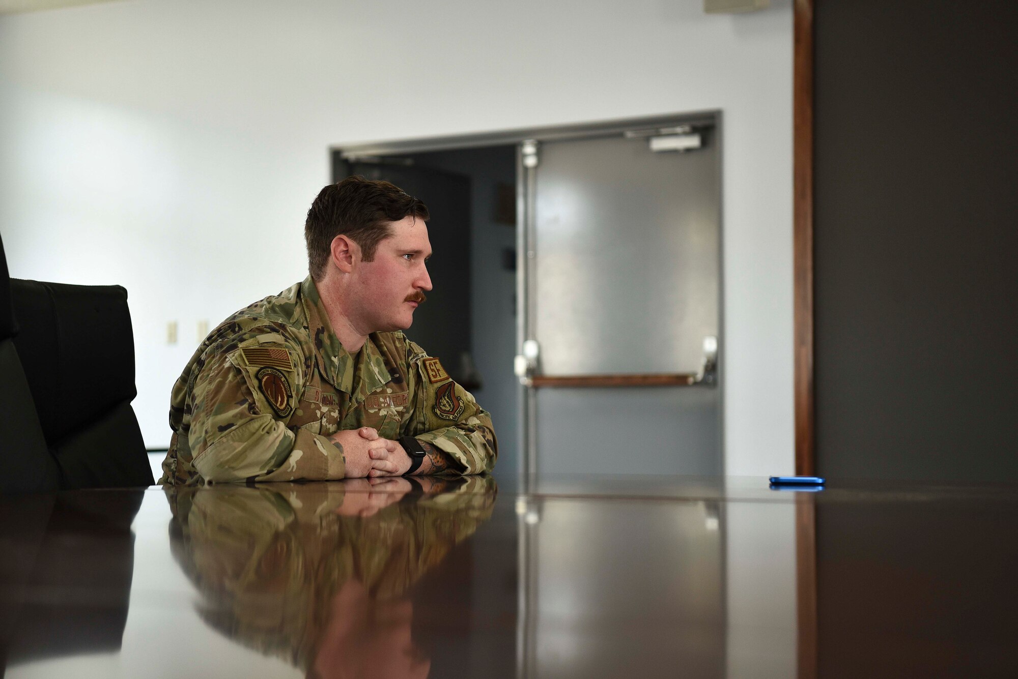 A military member holds his hands over a table looking ahead.